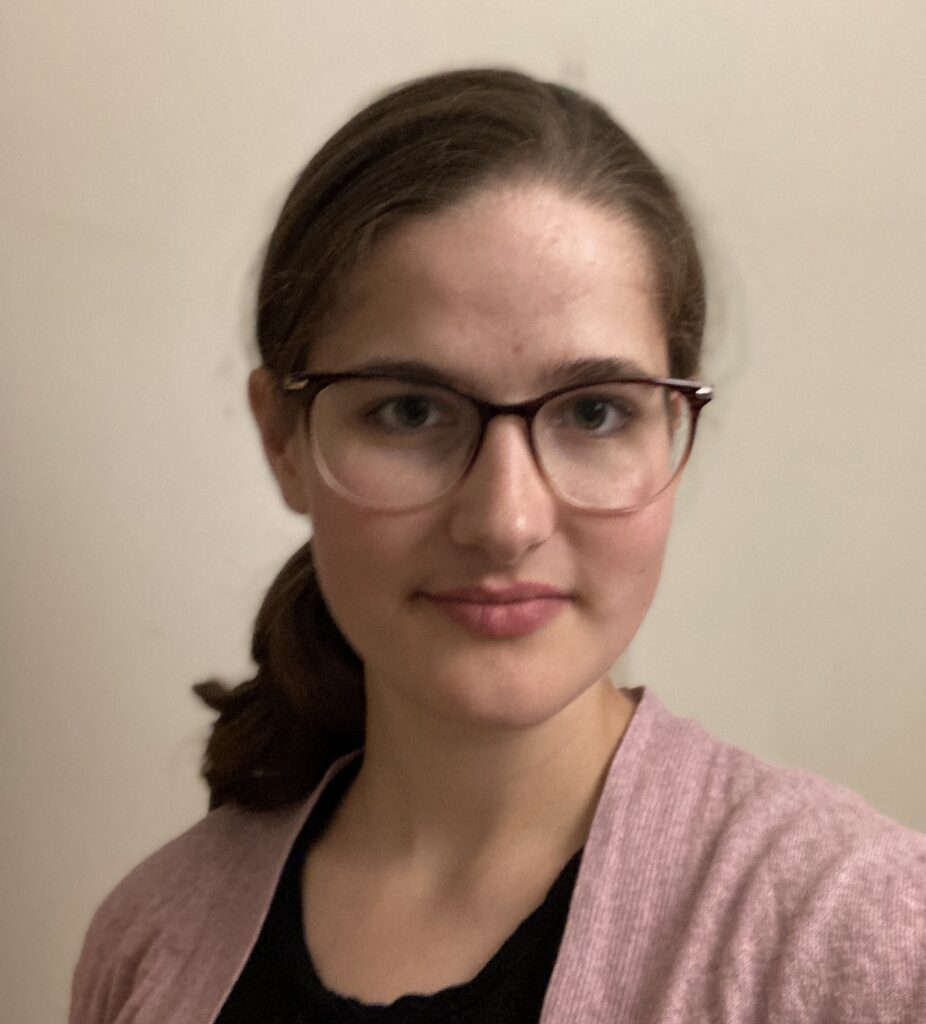 A headshot of Em, a white woman with brown hair and glasses smiling looking into a camera.